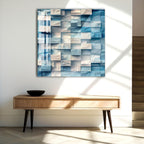 a modern art piece with a geometric pattern of blue and white squares on a white wall, hanging above a wooden console table with a black bowl on top.