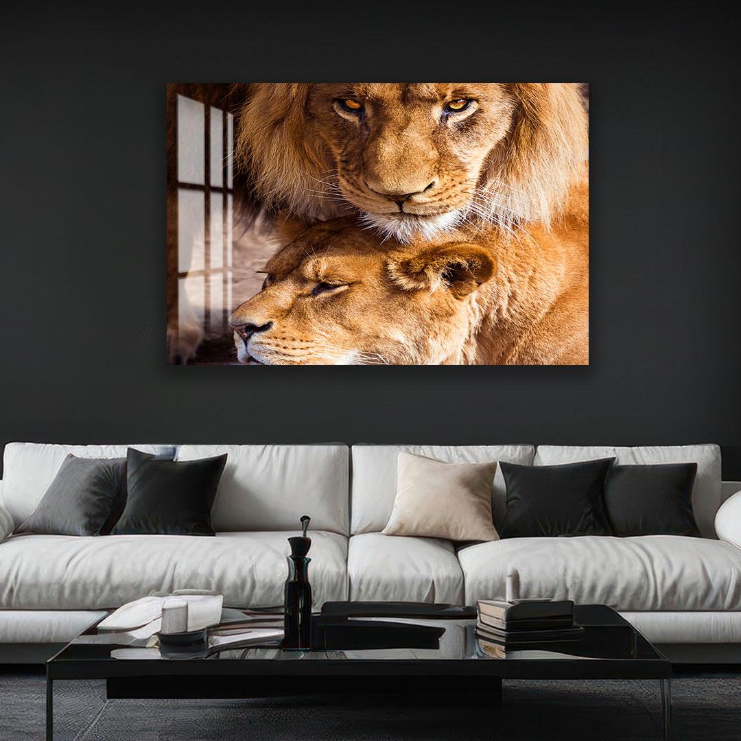 a large, striking photograph of two lions resting together on a couch. The lions are positioned close to each other, with one lying on top of the other, creating a sense of companionship and warmth. The photograph is displayed on a wall above a modern, minimalist living room setting, which includes a black coffee table and a white sofa.