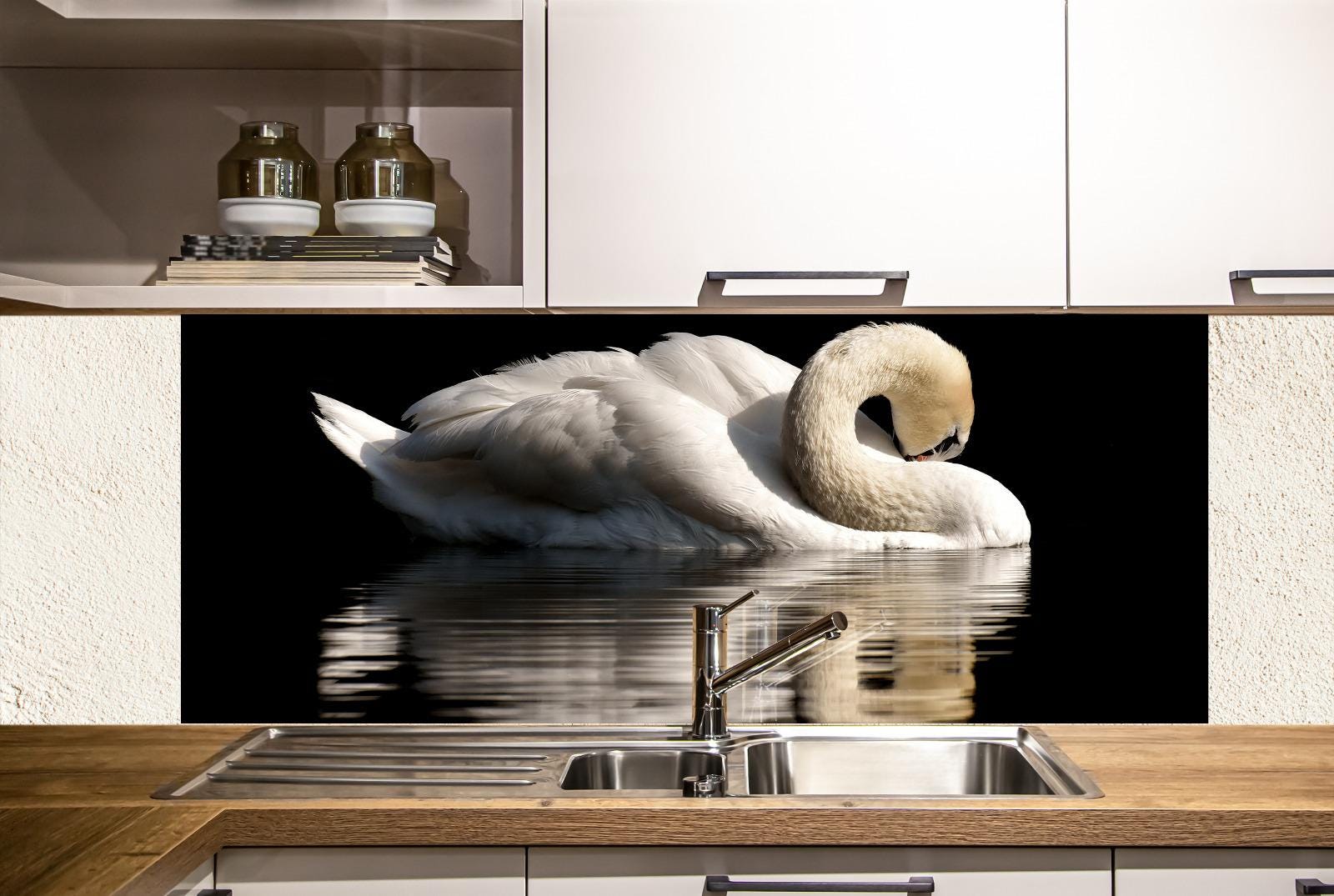 A white swan swimming in a reflective body of water, with a kitchen sink and cabinets visible in the foreground.
