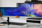 a modern kitchen with a striking blue and purple abstract mural on the wall behind the stove. The kitchen has white cabinets and a black oven, creating a clean and contemporary look. On the countertop, there are a few oranges and a wooden cutting board.