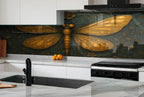 a kitchen with a large, detailed dragonfly mural on the wall behind the stove. The dragonfly has golden wings and a black body, and it is surrounded by green leaves and flowers. The kitchen has white cabinets and a black stove, and there are some oranges and a cutting board on the counter.