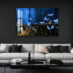 A tiger is drinking from a pond in a lush green forest, as depicted in a large framed artwork hanging on a dark wall above a white sofa in a modern living room setting.