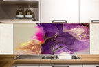 a kitchen with a large, colorful abstract mural painted on the wall behind the sink. The mural has a purple and gold color scheme, with swirling patterns and shapes that create a vibrant and dynamic visual effect. The kitchen has white cabinets and a wooden countertop, providing a clean and modern aesthetic.