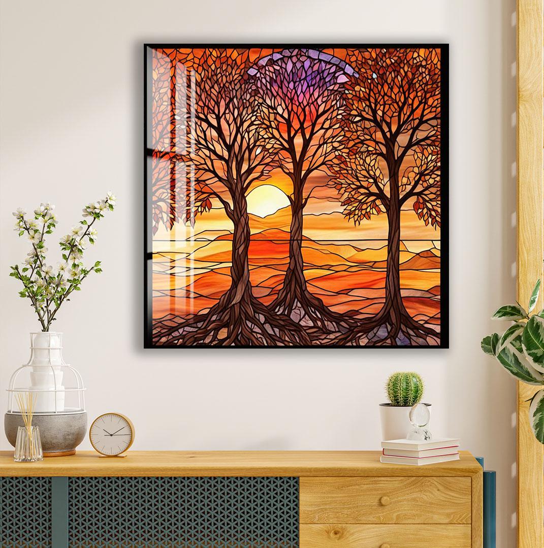 a framed stained glass artwork depicting a serene landscape with three trees with roots extending into the ground, set against a sunset-like background. The artwork is hung on a wall above a wooden dresser, which also holds a clock, a vase with flowers, and a stack of books.