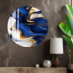 a large circular wall art piece with a swirling pattern of blue and gold colors, hanging on a wall next to a wooden shelf with a lamp and a plant.