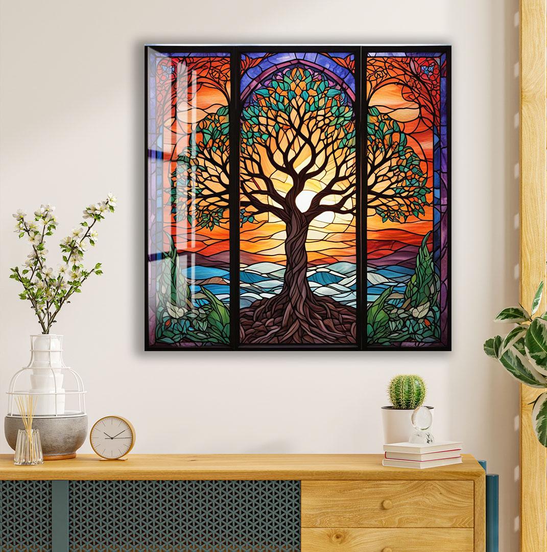 a large, colorful stained glass window depicting a tree with a vibrant, sun-like design in the center. The window is divided into three panels, each showcasing different elements of the tree and its surroundings. The window is mounted on a wall above a wooden dresser, which also holds a clock, a vase with flowers, and a stack of books.