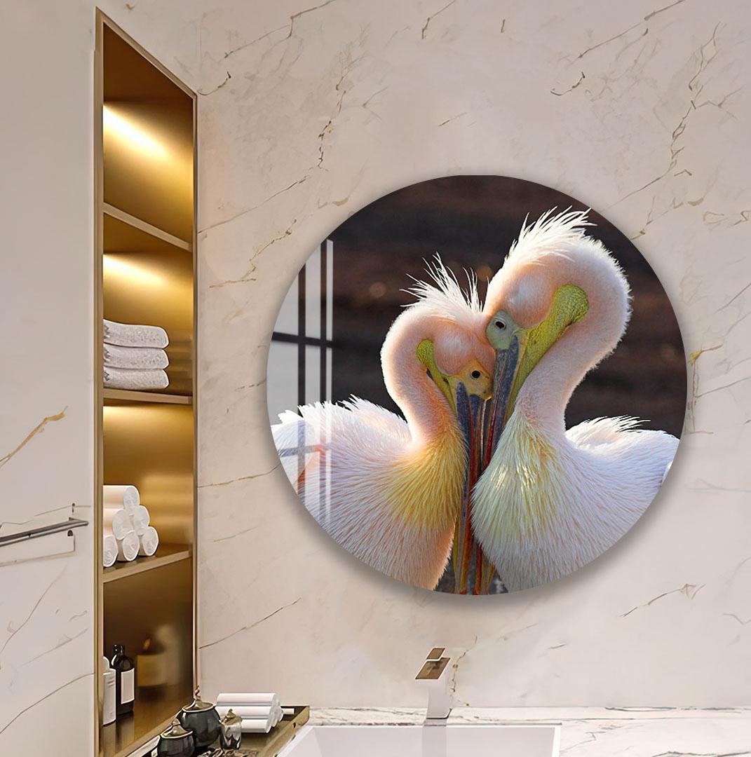 A round mirror in a bathroom displays a photograph of two pelicans standing close together, with their heads almost touching.