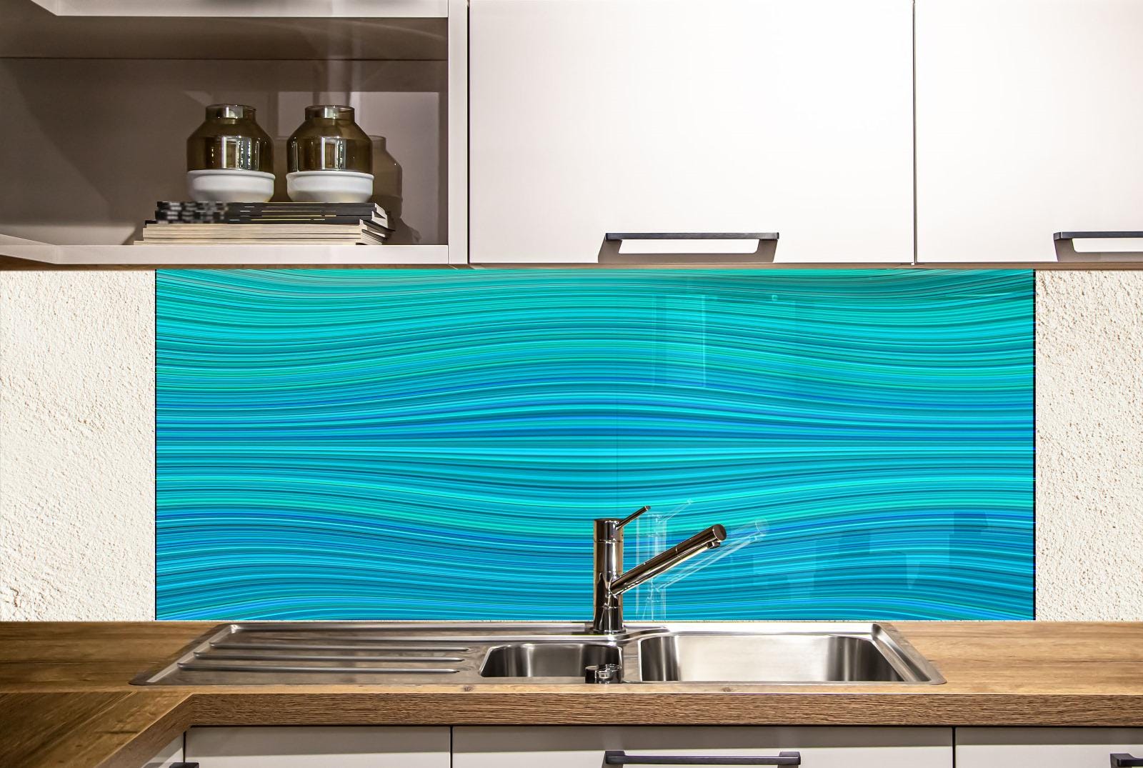 a modern kitchen with a blue and turquoise wave-patterned backsplash behind a stainless steel sink. The kitchen has white cabinets and a wooden countertop.