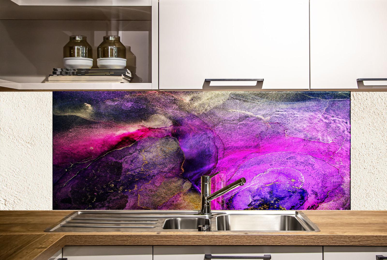 a kitchen with a colorful backsplash behind the sink, which has a vibrant abstract design in shades of purple, pink, and blue. The sink is positioned under the backsplash, and there are white cabinets above it. On the countertop, there are two bottles and a book, suggesting a functional and organized kitchen space.