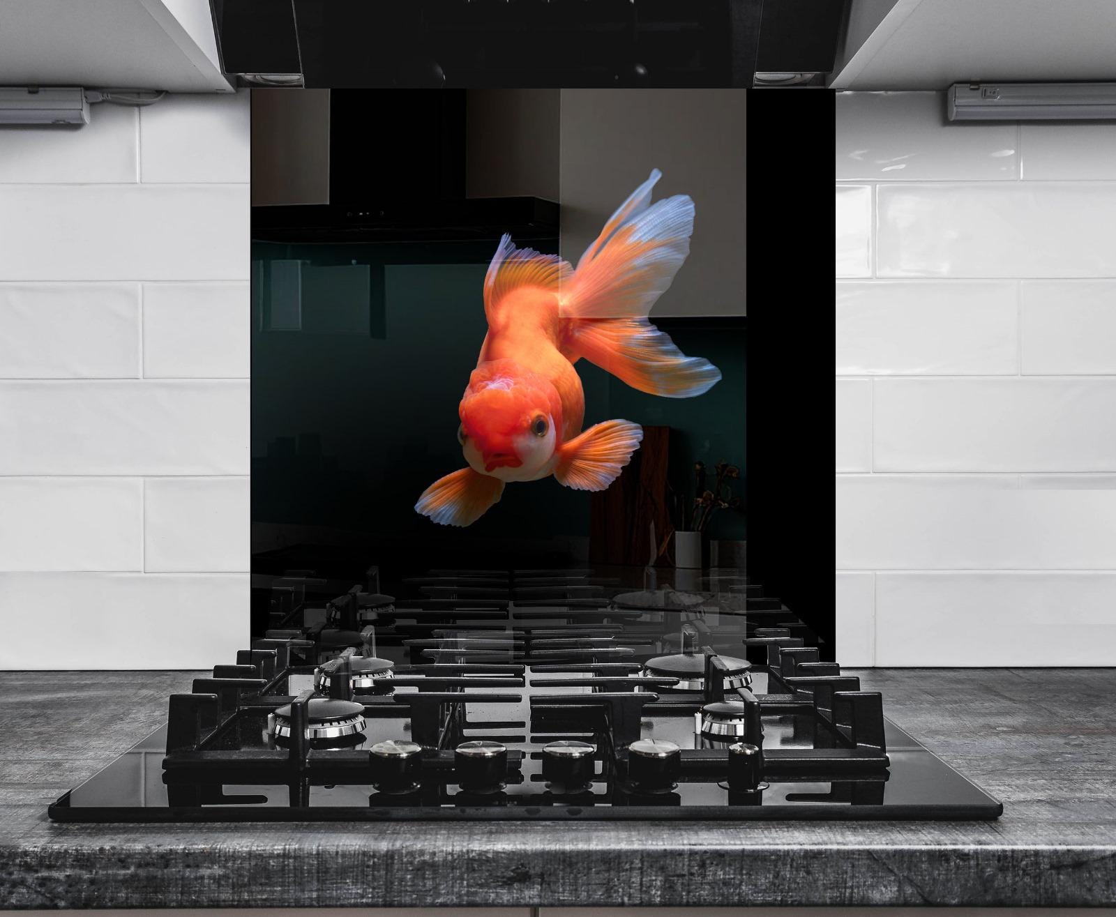 A vibrant orange goldfish is captured in mid-swim, its fins spread wide, against a backdrop of a black stovetop and white tiled wall.